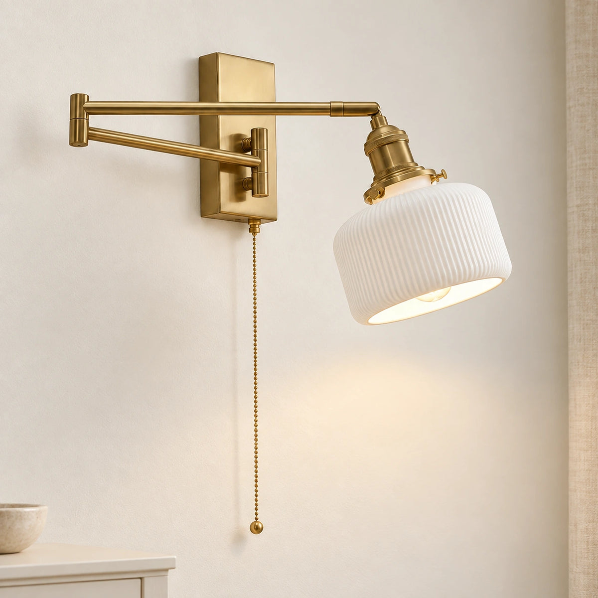 Estelle brass swing arm wall light switched on against a simple ivory wall